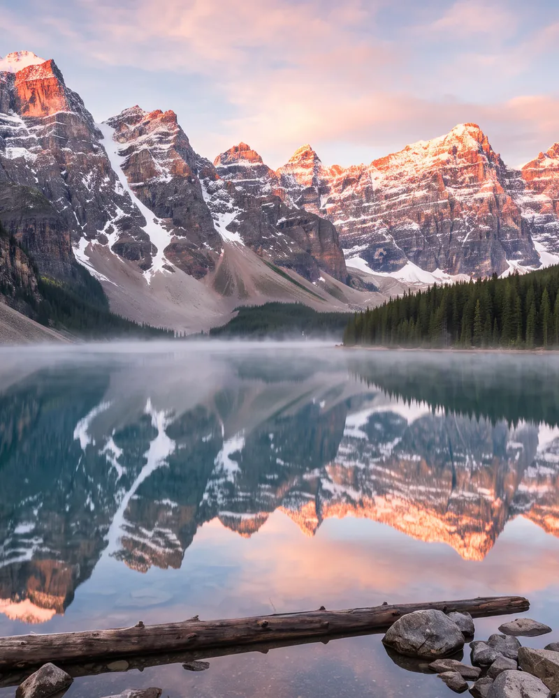 A calm alpine lake at dawn reflecting snow-capped peaks